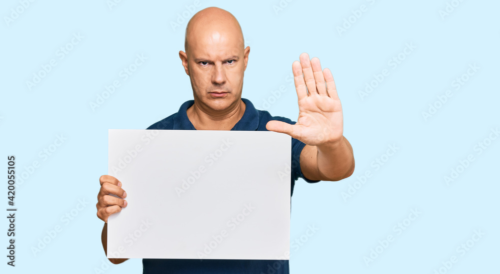 Middle age bald man holding blank empty banner with open hand doing stop sign with serious and confident expression, defense gesture Middle age bald man holding blank empty banner with open hand doing stop sign with serious and confident expression, defense gesture