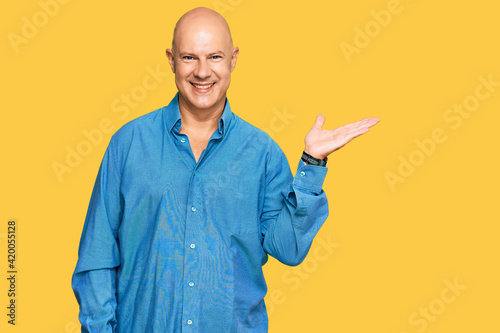 Middle age bald man wearing casual clothes smiling cheerful presenting and pointing with palm of hand looking at the camera.
