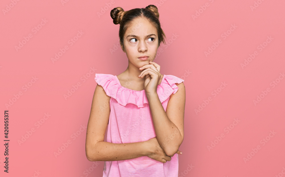 Beautiful brunette little girl wearing summer pink shirt serious face thinking about question with hand on chin, thoughtful about confusing idea Beautiful brunette little girl wearing summer pink shirt serious face thinking about question with hand on chin, thoughtful about confusing idea