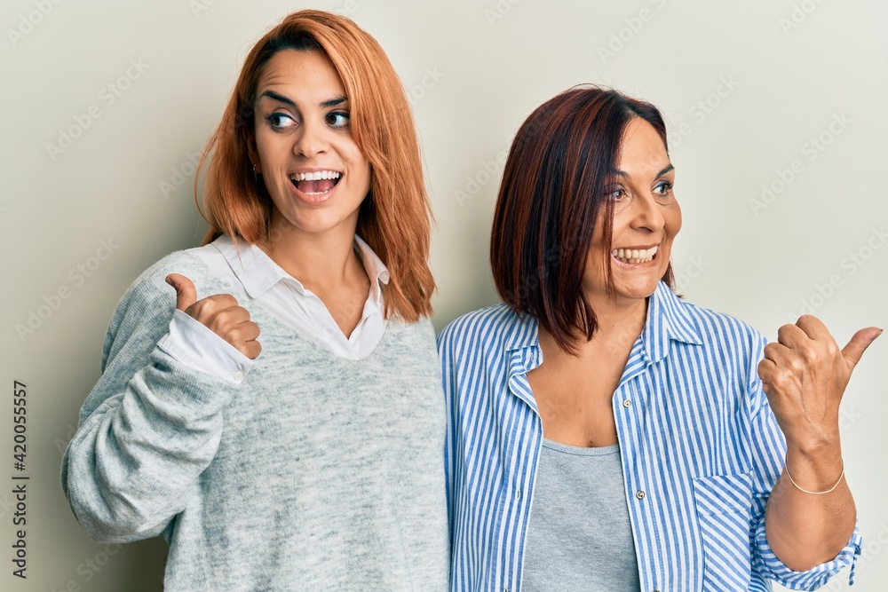 Latin mother and daughter wearing casual clothes pointing thumb up to the side smiling happy with open mouth Latin mother and daughter wearing casual clothes pointing thumb up to the side smiling happy with open mouth