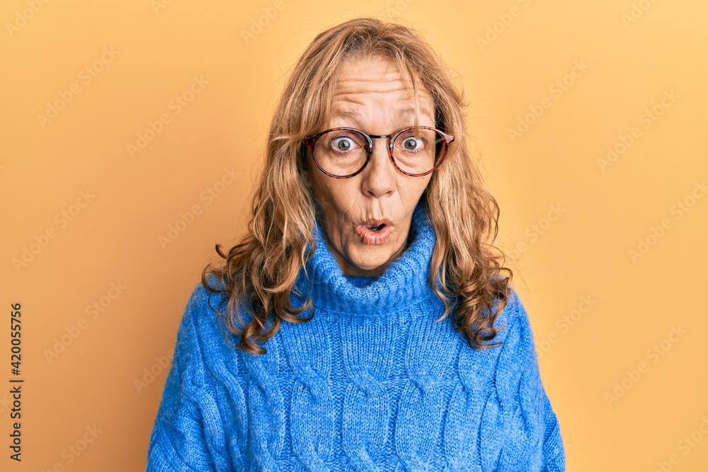 Middle age blonde woman wearing glasses and casual winter sweater afraid and shocked with surprise expression, fear and excited face.