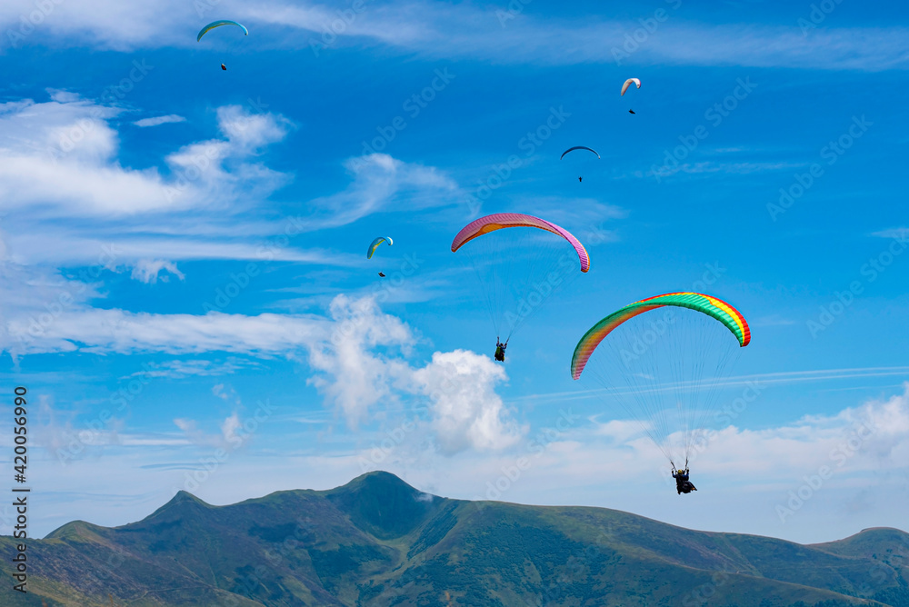 Young people fly paragliders in summer in the Carpathian mountains against a beautiful blue sky, people feel free and enjoy the view from above on landscapes
