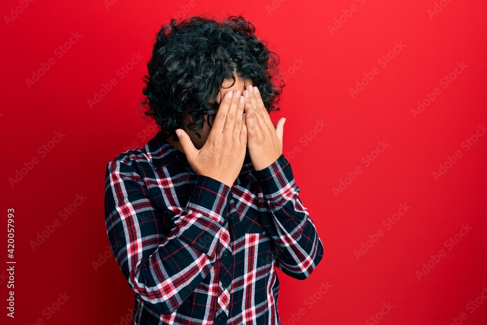 Young hispanic woman with curly hair wearing casual clothes and glasses with sad expression covering face with hands while crying. depression concept. Young hispanic woman with curly hair wearing casual clothes and glasses with sad expression covering face with hands while crying. depression concept.