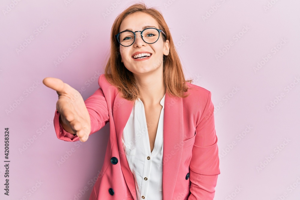Young caucasian woman wearing business style and glasses smiling friendly offering handshake as greeting and welcoming. successful business.