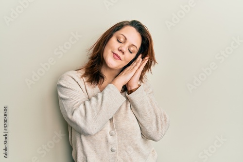 Young caucasian woman wearing casual clothes sleeping tired dreaming and posing with hands together while smiling with closed eyes.