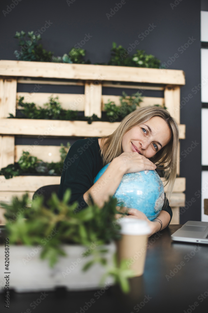 pretty young blonde woman with globe sits in front of laptop in a very modern, ecological, sustainable office and dreams of vacation, travel and the end of Corona pretty young blonde woman with globe sits in front of laptop in a very modern, ecological, sustainable office and dreams of vacation, travel and the end of Corona