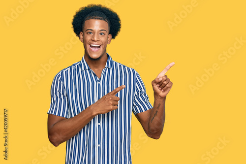 African american man with afro hair wearing casual clothes smiling and looking at the camera pointing with two hands and fingers to the side.