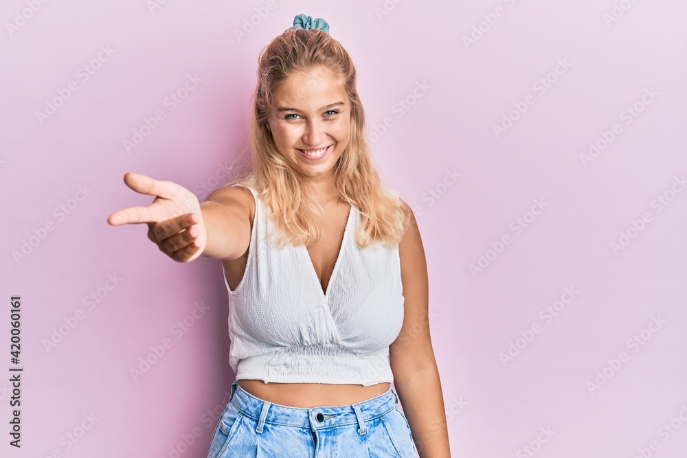Young blonde girl wearing casual clothes smiling friendly offering handshake as greeting and welcoming. successful business. Young blonde girl wearing casual clothes smiling friendly offering handshake as greeting and welcoming. successful business.