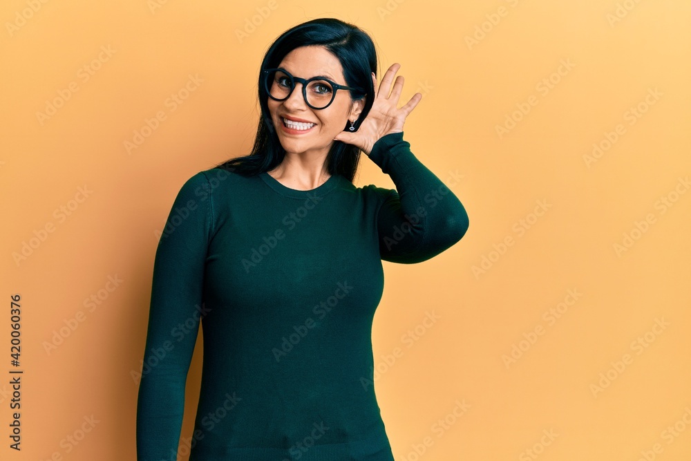Young caucasian woman wearing casual clothes and glasses smiling with hand over ear listening an hearing to rumor or gossip. deafness concept. Young caucasian woman wearing casual clothes and glasses smiling with hand over ear listening an hearing to rumor or gossip. deafness concept.