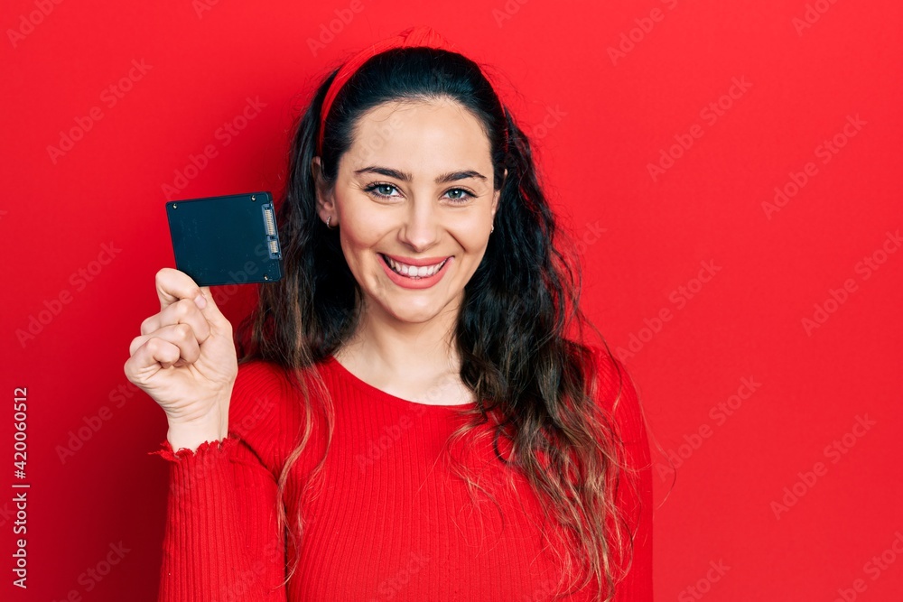 Naklejka premium Young hispanic woman holding ssd memory looking positive and happy standing and smiling with a confident smile showing teeth