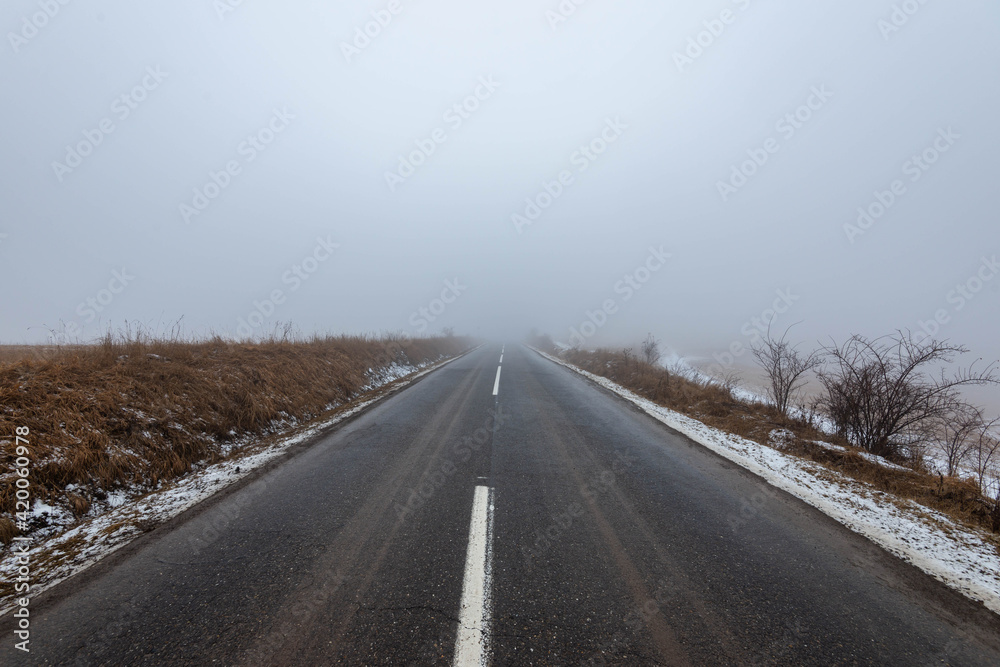 Asphalt road leading to the top of the hill at wintertime in dense fog with low visibility. Asphalt road leading to the top of the hill at wintertime in dense fog with low visibility.