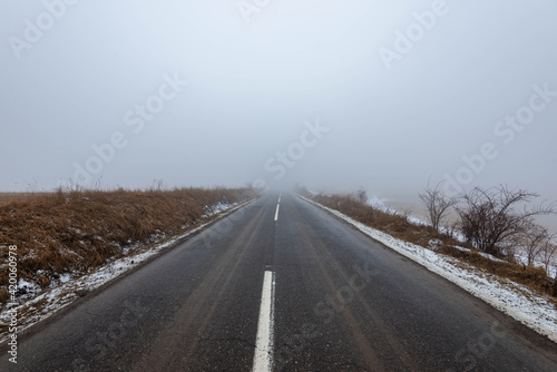 Asphalt road leading to the top of the hill at wintertime in dense fog with low visibility.