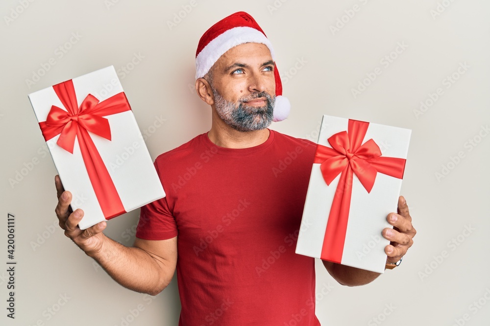 Middle age handsome man wearing christmas hat and holding a gifts smiling looking to the side and staring away thinking. Middle age handsome man wearing christmas hat and holding a gifts smiling looking to the side and staring away thinking.