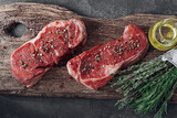 fresh raw striploin steak on a wooden board on a wooden background with salt and pepper in a rustic style.
