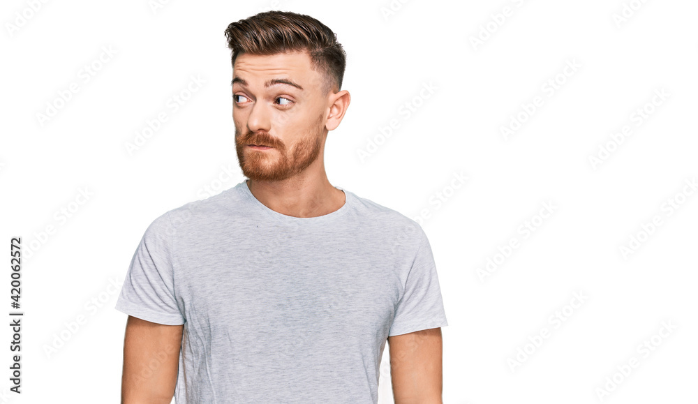 Young redhead man wearing casual grey t shirt smiling looking to the side and staring away thinking. Young redhead man wearing casual grey t shirt smiling looking to the side and staring away thinking.