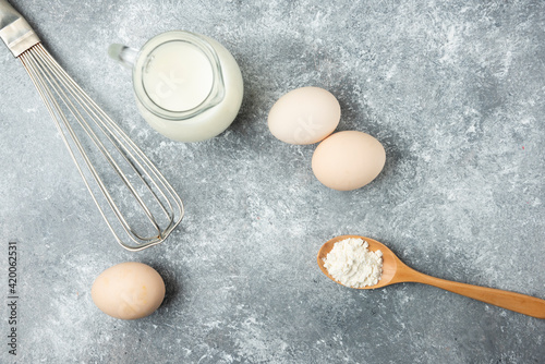 Bowl of flour, eggs and whisker on marble background
