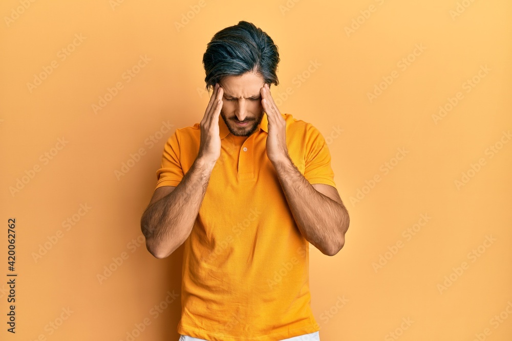 Young hispanic man wearing casual yellow t shirt with hand on head for pain in head because stress. suffering migraine. Young hispanic man wearing casual yellow t shirt with hand on head for pain in head because stress. suffering migraine.