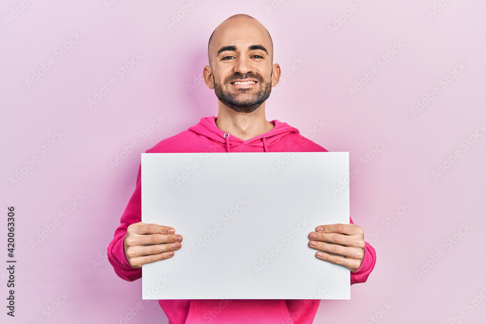 Young bald man holding blank empty banner smiling with a happy and cool smile on face. showing teeth. Young bald man holding blank empty banner smiling with a happy and cool smile on face. showing teeth.
