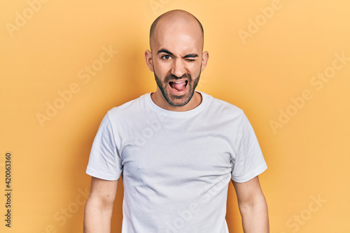 Young bald man wearing casual white t shirt winking looking at the camera with sexy expression, cheerful and happy face.