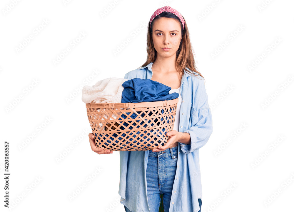 Young beautiful girl holding laundry basket thinking attitude and sober expression looking self confident Young beautiful girl holding laundry basket thinking attitude and sober expression looking self confident