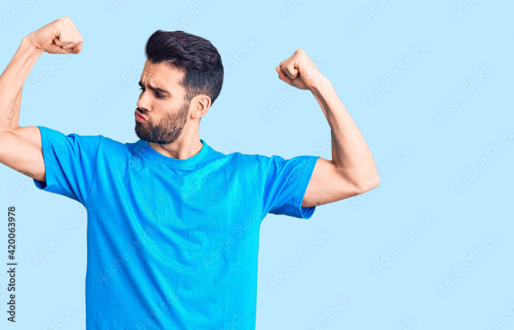 Fototapeta premium Young handsome man with beard wearing casual t-shirt showing arms muscles smiling proud. fitness concept.