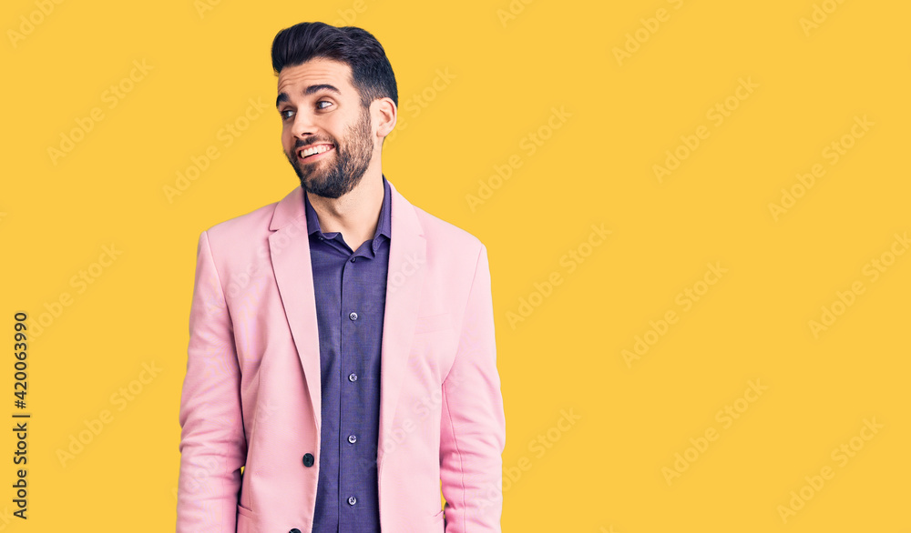 Young handsome man with beard wearing elegant jacket looking away to side with smile on face, natural expression. laughing confident.
