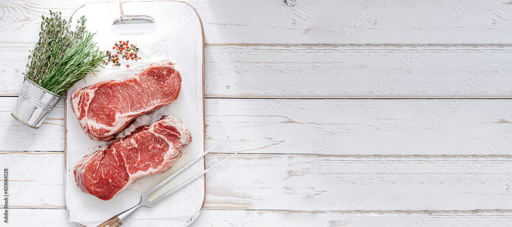 fresh raw striploin steak on a white wooden board on a wooden background with salt and pepper in a rustic style.