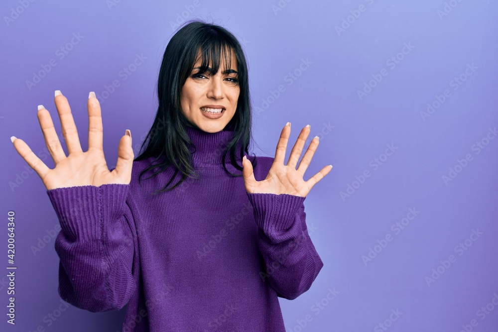 Young brunette woman with bangs wearing turtleneck sweater afraid and terrified with fear expression stop gesture with hands, shouting in shock. panic concept. Young brunette woman with bangs wearing turtleneck sweater afraid and terrified with fear expression stop gesture with hands, shouting in shock. panic concept.
