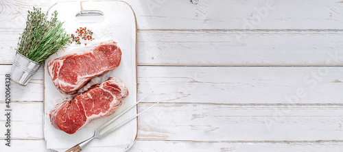 Obraz na płótnie fresh raw striploin steak on a white wooden board on a wooden background with salt and pepper in a rustic style. w salonie