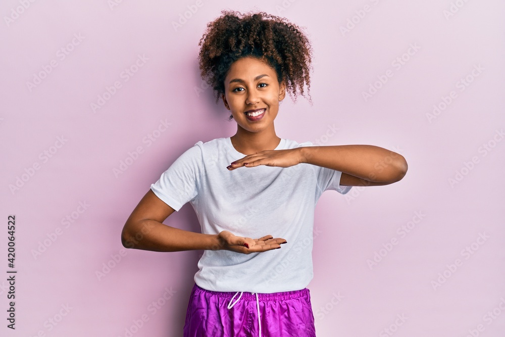 Beautiful african american woman with afro hair wearing sportswear gesturing with hands showing big and large size sign, measure symbol. smiling looking at the camera. measuring concept. Beautiful african american woman with afro hair wearing sportswear gesturing with hands showing big and large size sign, measure symbol. smiling looking at the camera. measuring concept.