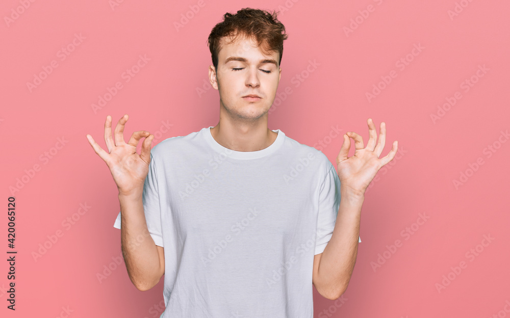 Young caucasian man wearing casual white t shirt relax and smiling with eyes closed doing meditation gesture with fingers. yoga concept. Young caucasian man wearing casual white t shirt relax and smiling with eyes closed doing meditation gesture with fingers. yoga concept.