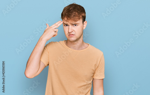 Young caucasian man wearing casual clothes shooting and killing oneself pointing hand and fingers to head like gun, suicide gesture.