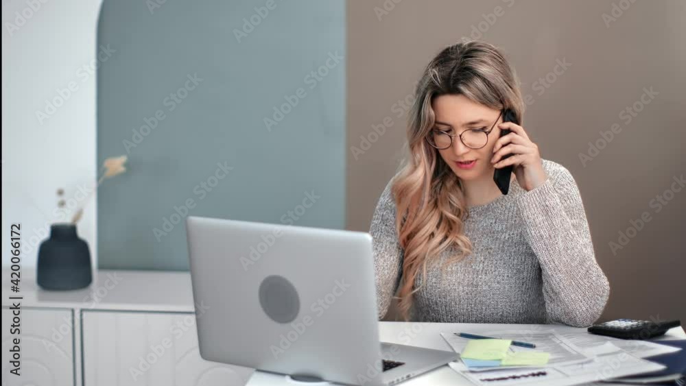 Busy feminine talking use smartphone working at desk with laptop. Shot on RED Raven 4k Cinema Camera Busy feminine talking use smartphone working at desk with laptop. Shot on RED Raven 4k Cinema Camera