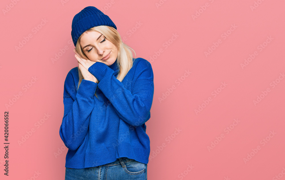 Young caucasian woman wearing wool winter sweater and cap sleeping tired dreaming and posing with hands together while smiling with closed eyes.