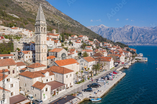 Aerial shot of the old coastal town of Perast at the foot of the mountain. Seaside promenade, residential buildings with traditional balkan red roofs, ancient Cathedral and coastline