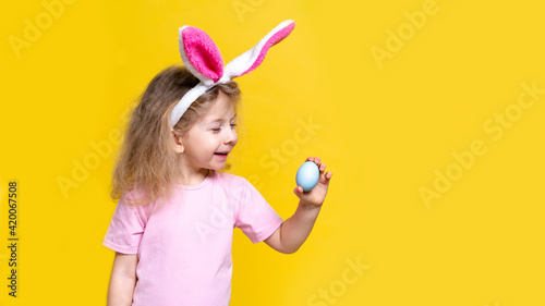 a little blonde girl with Easter bunny ears and Easter colored eggs on a yellow background with space for text