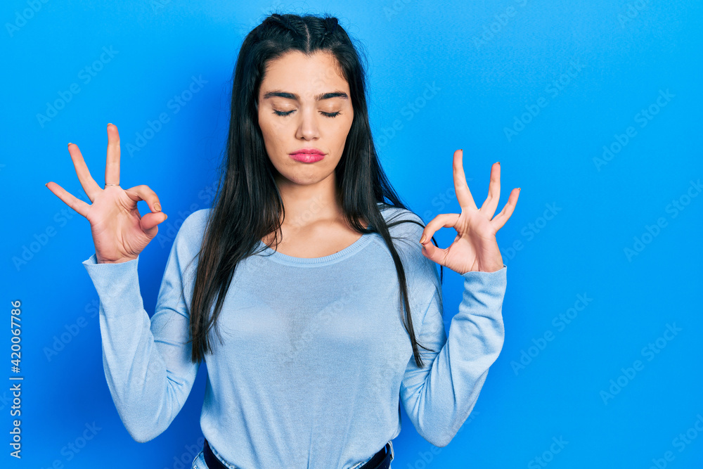 Young hispanic girl wearing casual clothes relax and smiling with eyes closed doing meditation gesture with fingers. yoga concept. Young hispanic girl wearing casual clothes relax and smiling with eyes closed doing meditation gesture with fingers. yoga concept.