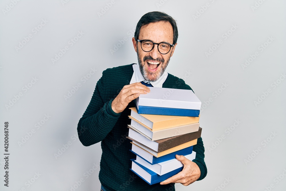 Middle age hispanic man holding a pile of books smiling and laughing hard out loud because funny crazy joke. Middle age hispanic man holding a pile of books smiling and laughing hard out loud because funny crazy joke.