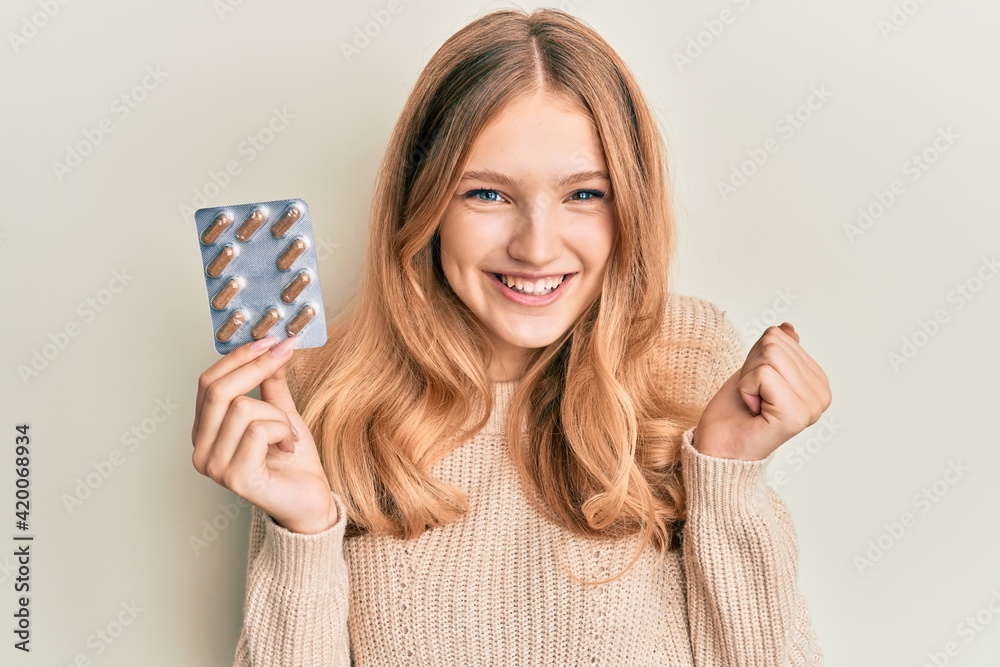 Beautiful young caucasian girl holding pills screaming proud, celebrating victory and success very excited with raised arm Beautiful young caucasian girl holding pills screaming proud, celebrating victory and success very excited with raised arm