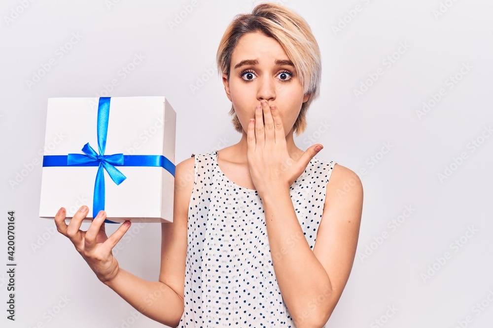 Young beautiful blonde woman holding gift covering mouth with hand, shocked and afraid for mistake. surprised expression Young beautiful blonde woman holding gift covering mouth with hand, shocked and afraid for mistake. surprised expression