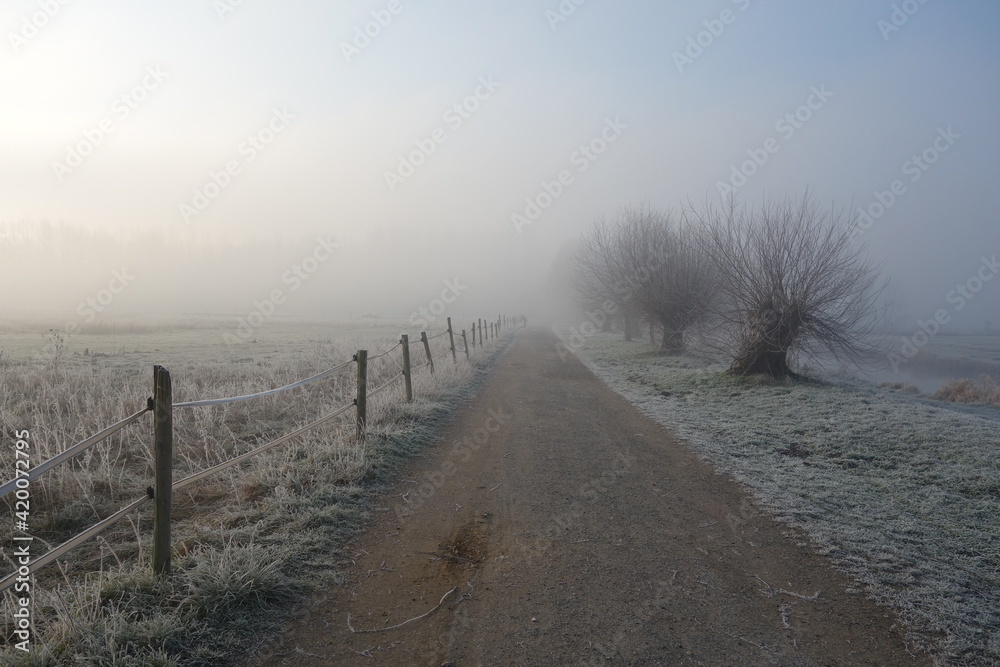 Weg am Niederrhein bei Grefrath Oedt mit Zaunpfählen bei Frost an einem Wintermorgen