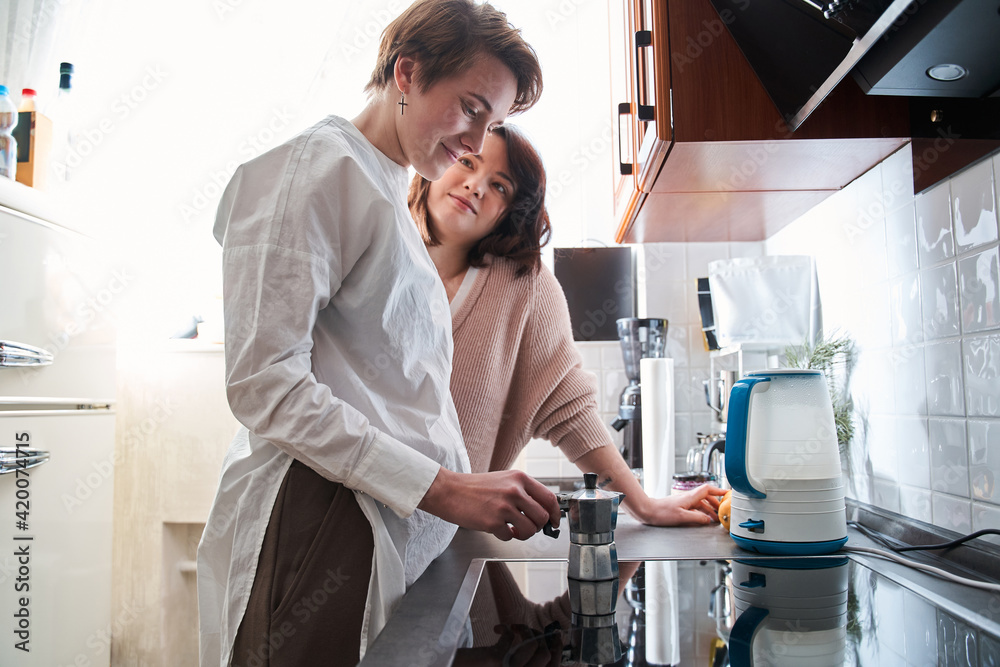 Beautiful young lesbian couple preparing coffee in the kitchen at home Beautiful young lesbian couple preparing coffee in the kitchen at home
