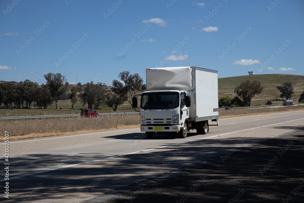 Truck on a freeway with plane flying overhead in Australian Country Town midway between Sydney and Melbourne with nice blue sky and lush green trees as a backdrop