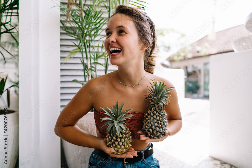 Laughing woman holding fresh pineapples - obrazy, fototapety, plakaty 
