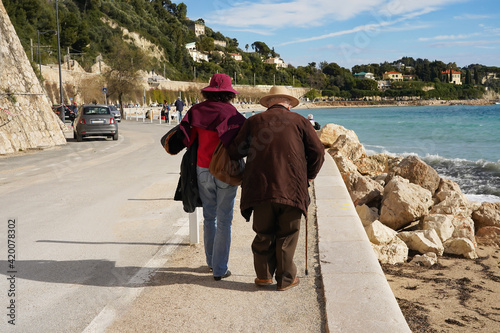 An elderly couple strolls along the promenade along the Mediterranean coast on a sunny spring day. South coast of France, Villefranche-sur-Mer.