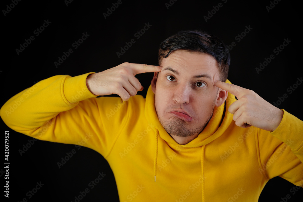 Portrait of young man in yellow hoodie with grimacing face. Close up of funny guy monkeying on black background. Portrait of young man in yellow hoodie with grimacing face. Close up of funny guy monkeying on black background.
