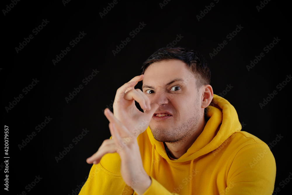 Portrait of young man in yellow hoodie with grimacing face. Close up of funny guy monkeying on black background. Portrait of young man in yellow hoodie with grimacing face. Close up of funny guy monkeying on black background.