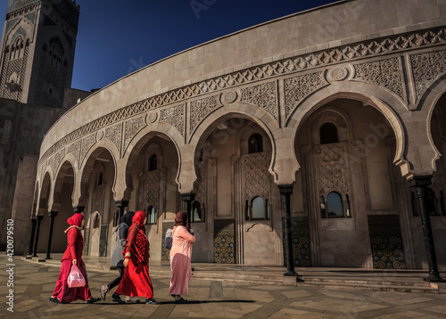 Eine Gruppe von muslimischen Frauen mit roten Gewändern und Hijab gehen zu den Arkaden der Hassan II Moschee in Casablanca Marokko