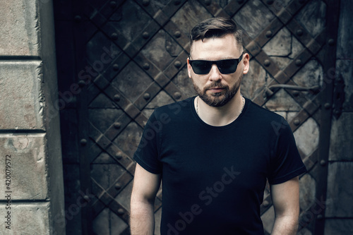 Portrait of a young handsome attractive bearded model man in sunglasses, black t-shirt, looking at camera. Stylish hipster.