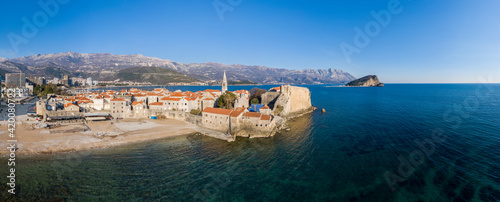 Aerial View of Budva Old Town and sandy beach in a beautiful spring day. Top view from drone on the old fortress and azure sea. Horizontal panorama, Montenegro